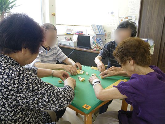 麻雀卓を囲んで4人の入居者が真剣に勝負している。窓が大きく明るい。