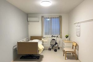 ベッドに横たわりほほ笑む高齢の女性と、その女性の手に触れながら話しかける女性スタッフの様子。