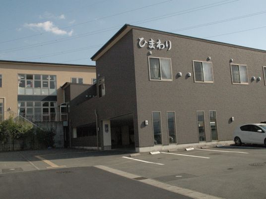 大きな駐車場が写っている施設の外観写真。シックな色合いの建物と広めの敷地内