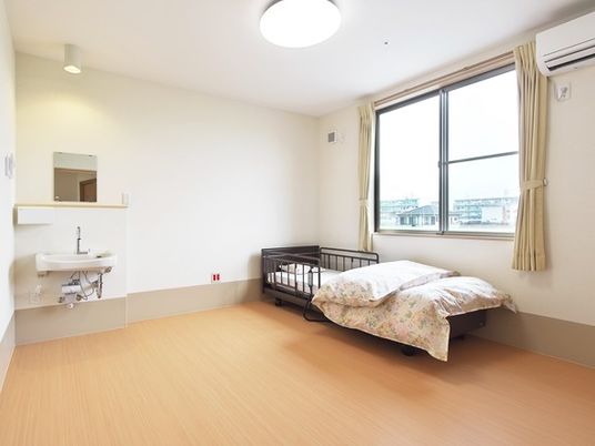寝具付きのベッドが置かれたフローリングの居室には洗面所もあり、大きな窓が付き明るい雰囲気。