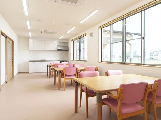 ピンクの椅子が4脚ずつセットされたダイニングテーブルが並んでいる食堂にはキッチンもある。
