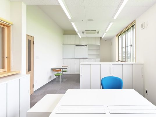 白を基調とした清潔感のある事務室。大きなデスクに青い椅子が1脚セットされている。