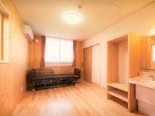 木製の収納棚やその横に洗面台が置いてある居室内。奥のほうにベッドとエアコンが写っている様子
