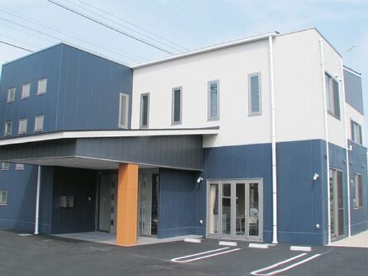 ブルーと白の外壁の２階建ての建物は玄関には屋根が付き、駐車場も設置されている。