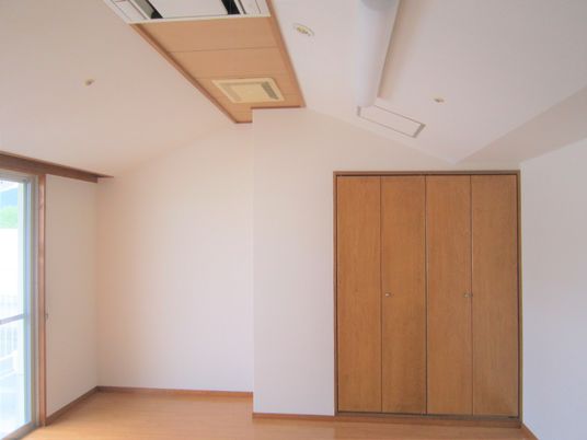 大きなクローゼットが付いたフローリングの部屋には大きなエアコンと窓があり、窓にはカーテンが付いていない。