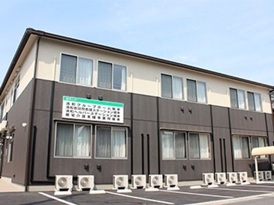 各フロアでが壁の色が異なる２階建ての建物の前には駐車スペースがあり、ホームや併設事業所名が書かれている。