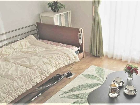 ベッドやテーブルが設置された家庭的な居室。大きな窓にはカーテンもついている。