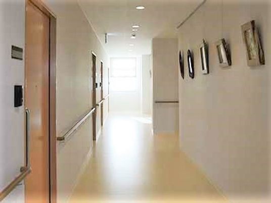 廊下の右側には絵画が飾られ、左側には居室が並び、奥には窓があり明るい雰囲気。