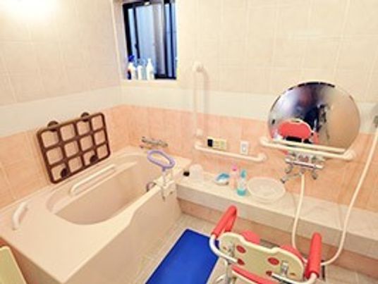 立ち上がり用の手すりやシャワーチェアがある浴室スペース。丸い鏡がある浴室