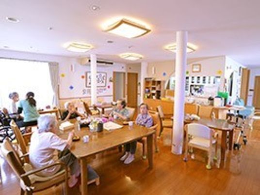 あたたかみあるフローリングのスペースといす、テーブル、そこに集う人々が写っている