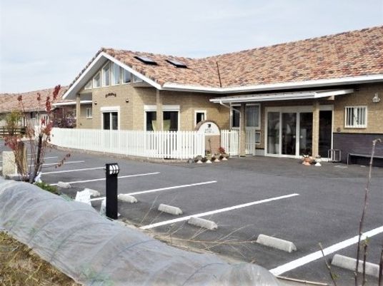 やわらかい色合いの外観が印象的な建物の外観。手前に駐車場スペースがある空間