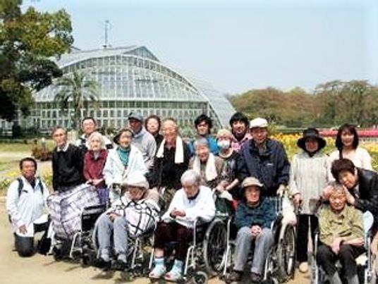 多くの高齢者がこちらを向いて微笑んでいる様子。施設のスタッフとその利用者の写真