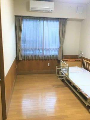 フローリング仕様の小さなワンルームタイプの部屋。介護用ベッドが置いてある様子