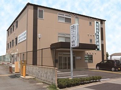 3階建ての建物はブラウン系で駐車場があり、ホーム名が書かれた看板も立っている。