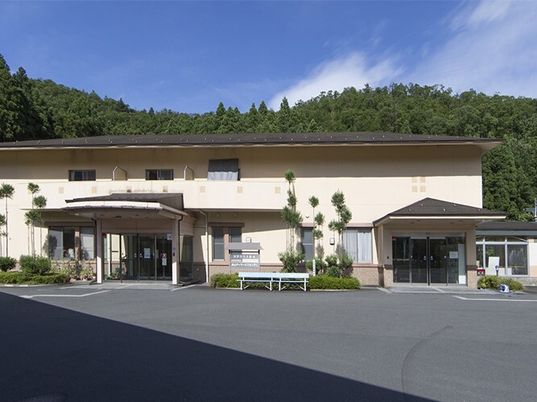 2階建ての建物は自然に囲まれ、大きな玄関が2か所に付き、広い駐車場があり、ベンチも置かれている。