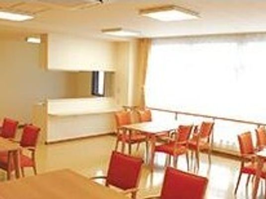 赤い椅子がセットされた４人掛けのダイニングテーブルが複数置かれた明るい雰囲気の食堂には、対面式キッチンも設置されている。