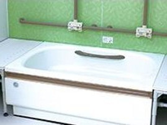 手すりが壁に設置され、一人用の浴槽の両サイドにベンチが付き、安全に配慮された浴室。壁はグリーンでさわやかな印象。
