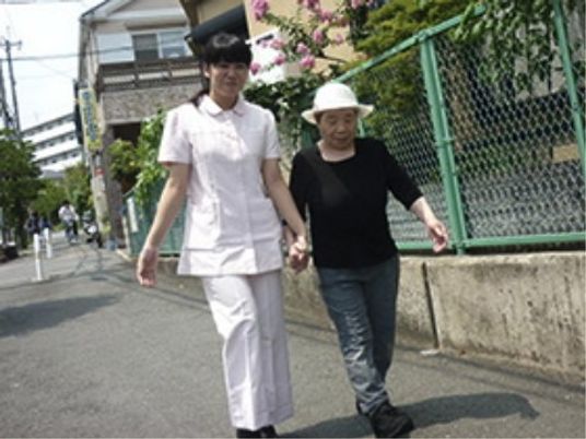白衣を着た女性スタッフと帽子をかぶった女性入居者が散歩を楽しんでいる様子。
