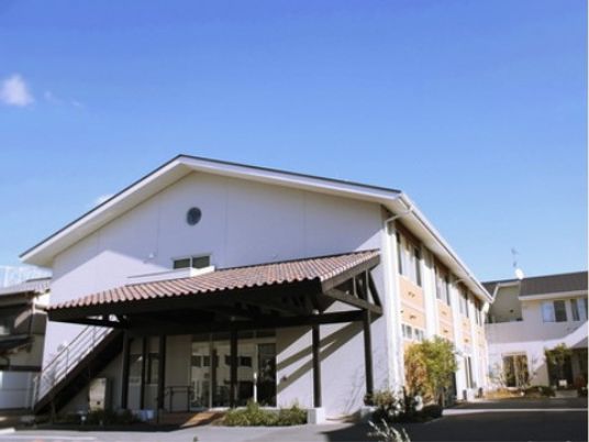 建物の玄関近くには屋外の避難用階段が設置され、屋根もついている。木や花が植えられたアットホームな雰囲気のホーム。
