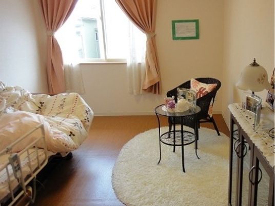 ベッドやテーブルセット、収納家具が置かれた居室。毛の長いカーペットや花柄のベッドカバーが自宅のような雰囲気。