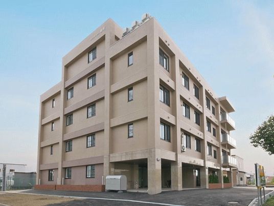 鉄骨造の背の高い建物の様子。マンション風の外観、駐車場スペースが写っている写真