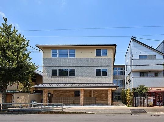 3階建ての建物はベージュとグレーで落ち着いた雰囲気。1階部分には駐車スペースもあり、道路に面している。