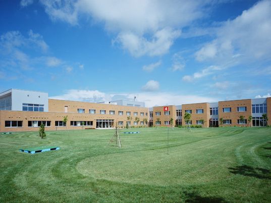 芝生のある広い空間に建物が並んでいる様子。薄雲が広がる青空の様子