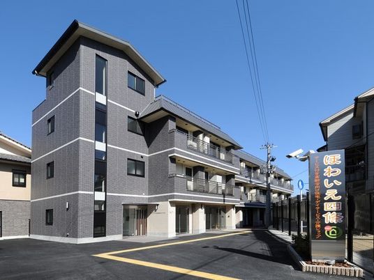 グレーの3階建ての建物にはベランダが付き、敷地の出入り口には看板も設置されている。