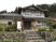 自然に囲まれた緑豊かな場所に建つ2階建ての民家風の住宅。瓦屋根で1階部分よりも2階部分が小さく、玄関の前の階段には手すりが付いている。