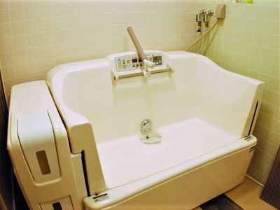 白い機械浴が置かれた浴室はタイル張り。機械浴にはたくさんのボタンが付いている。