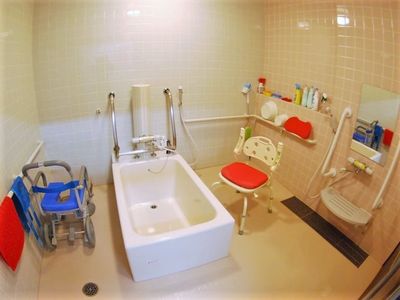洗い場が広い浴室には白い個浴槽と浴室用車いすやシャワーチェア、シャワーがある。