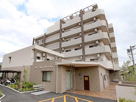 ベージュの建物は重厚感のあるデザインで玄関先にはベンチが置かれ、各フロアにベランダも付いている。