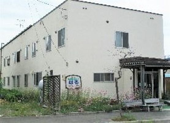 白を基調とした2階建ての建物。玄関先には屋根が付いていて、周辺には花畑がある。