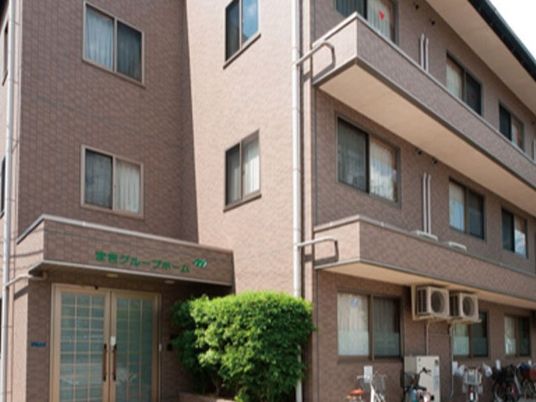 ブラウン系の外壁の３階建ての建物は日当たりがよく、玄関には屋根があり、ホーム名が書かれている。