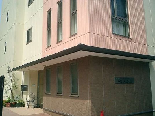 ピンクと白、茶色で彩られた建物のエントランス部分には椅子と植物が置かれている。