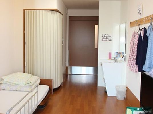 介護ベッドや車いす対応の洗面所があり、カーテンで仕切られているスペースがあり、服も数着かけられている。