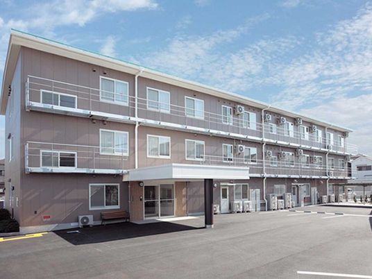 ３階建ての建物はグレー系の外壁で建物の建っている敷地内には広い駐車場があり、玄関先には車寄せが付いている。