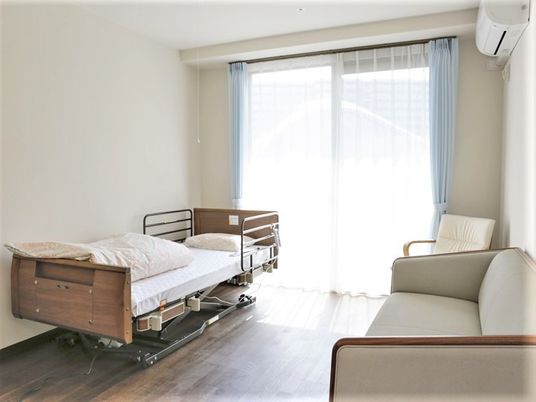ベッドとエアコン、ソファが置いてある小さなワンルームのの様子。施設内の居室空間