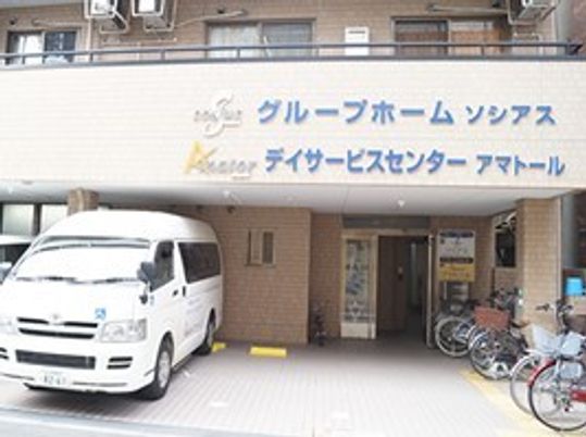 グループホームソシアスとデイサービスセンターの外観写真。車が置いてあるスペース