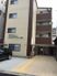 ベージュとブラウンの4階建ての建物の前には駐車場があり、車が止められている。玄関前まで点字ブロックが敷かれている