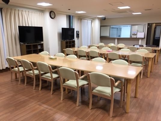 大きなダイ二ングテーブルが3組置かれた広い食堂にはテレビも2台置かれ、奥にはキッチンもある。