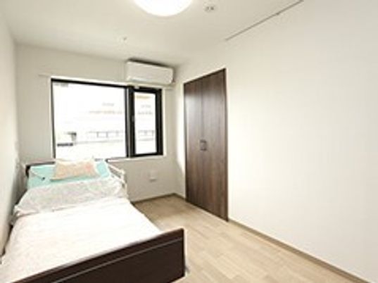 ベッドやクローゼット、エアコンが設置されたフローリングの部屋には大きな窓がある。