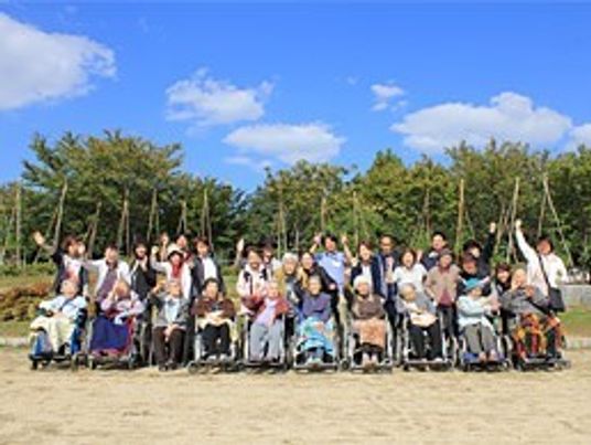 青空の下で外出イベントを楽しむ入居者とスタッフ。車いすの入居者もいる。