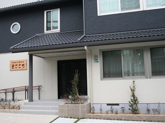 2階建ての建物はモノトーンで和モダンの雰囲気。玄関には屋根が付き、手すり付きのスロープや階段もある。