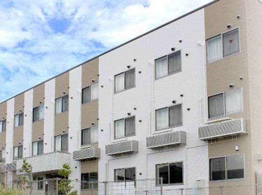 縦にツートンカラーを施したやわらかい色合いの建物。サービス付き住宅ひまわりの外観写真