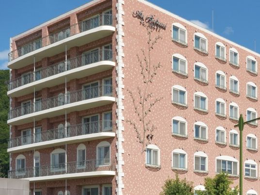 ブラウン系の大きな建物の外壁には木の絵が描かれ、窓もたくさんある。各フロアにベランダがあり、日当たりも良好。