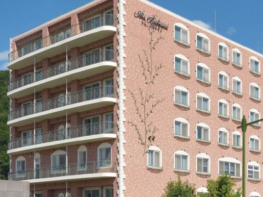 ブラウン系の大きな建物の外壁には木の絵が描かれ、窓もたくさんある。各フロアにベランダがあり、日当たりも良好。
