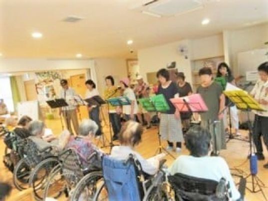 多くの高齢者とスタッフ、ボランティアの人々が歌を一緒に歌っている様子