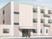 ベージュ系の建物は3階建てで、玄関には屋根が付いていて、その前には3名の人がいて話をしている。
