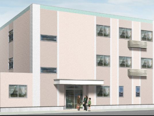 ベージュ系の建物は3階建てで、玄関には屋根が付いていて、その前には3名の人がいて話をしている。